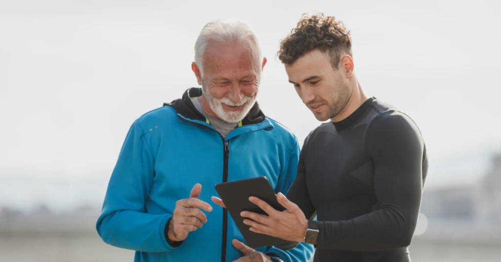 An older man in a blue jacket and a younger man look at a tablet screen together while researching daytime care options