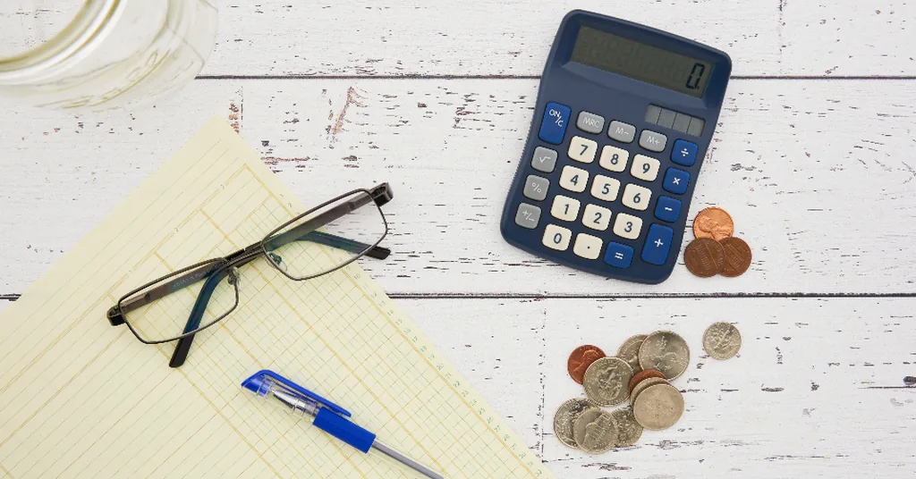 Calculator, coins, reading glasses and a notepad on a table, used to work out the monthly cost of assisted living